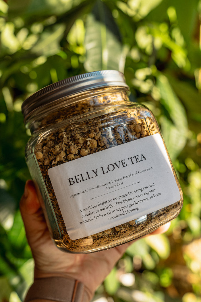 Jar of 'Belly Love Tea' held in a hand with a blurred green leafy background
