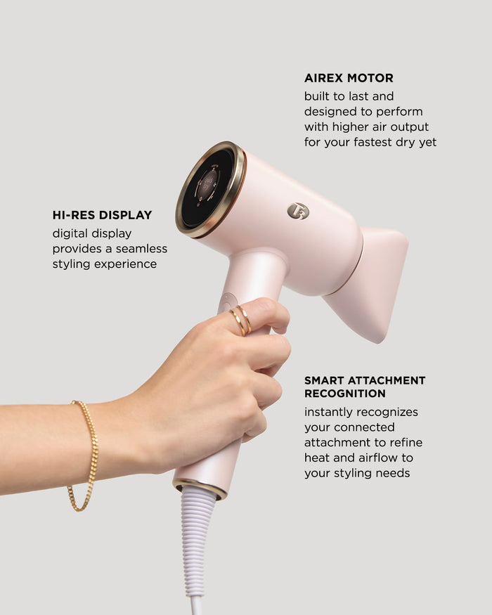 Hand holding a pink hair dryer with text highlighting features on a light gray background