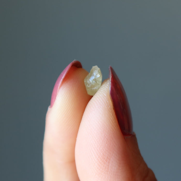 fingers holding a raw green apatite stone
