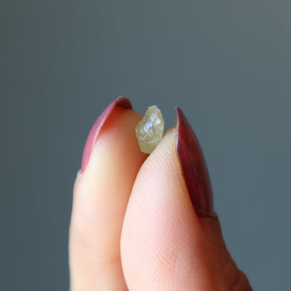 fingers holding a raw green apatite stone