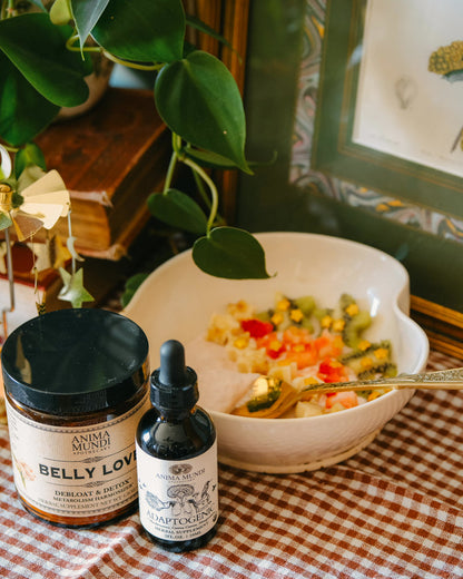 Two bottles on a checkered tablecloth with a bowl of food and plant in the background