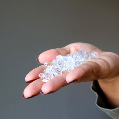 holding many Double Terminated Raw Clear Quartz gemstones in palm