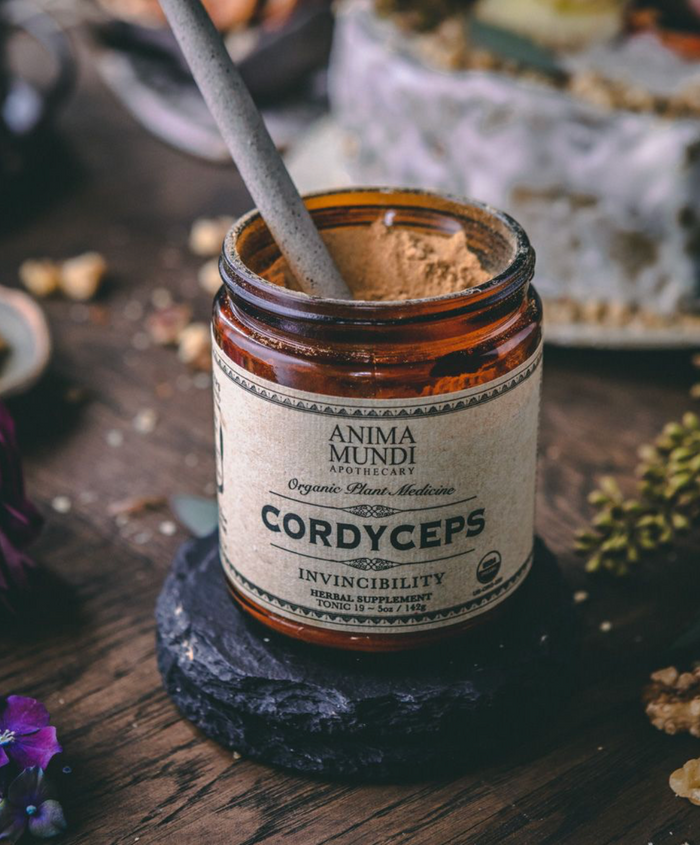 Jar of Anima Mundi Cordyceps supplement on a wooden surface with blurred background