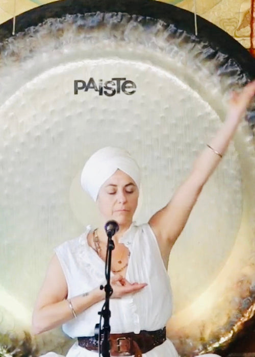 Person playing a large Paiste gong in front of a brick wall.
