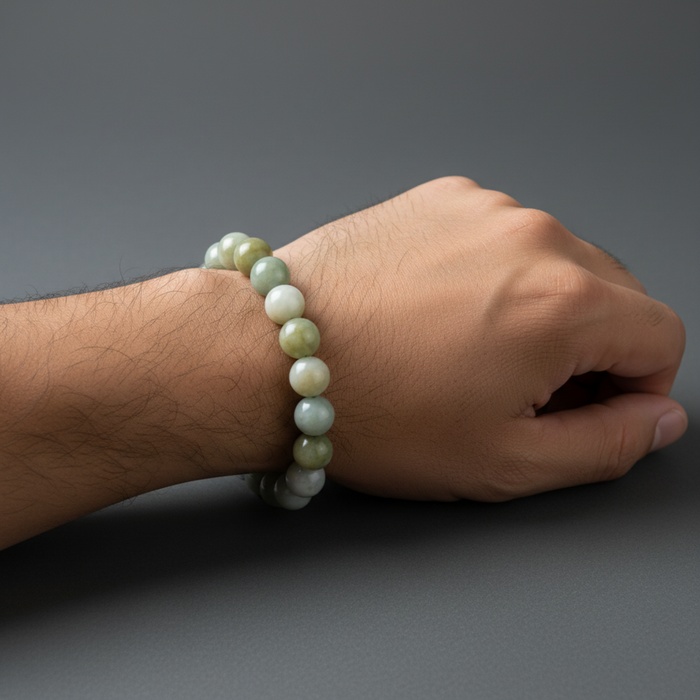 Hand wearing a green jade beaded bracelet on a gray background