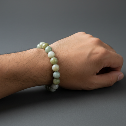 Hand wearing a green jade beaded bracelet on a gray background