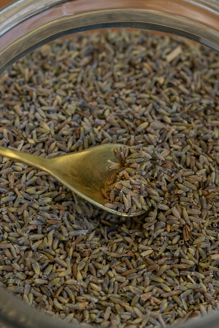 Close-up of a spoonful of dried lavender flowers over a jar filled with lavender.