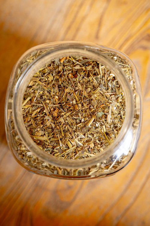 Glass jar filled with dried herbs on a wooden surface