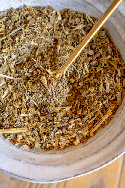 Herbal mix in a bowl with a gold spoon on a wooden surface