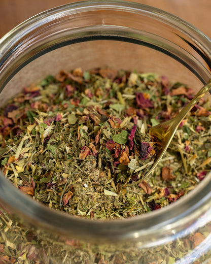 Glass jar filled with dried herbs and a gold spoon inside