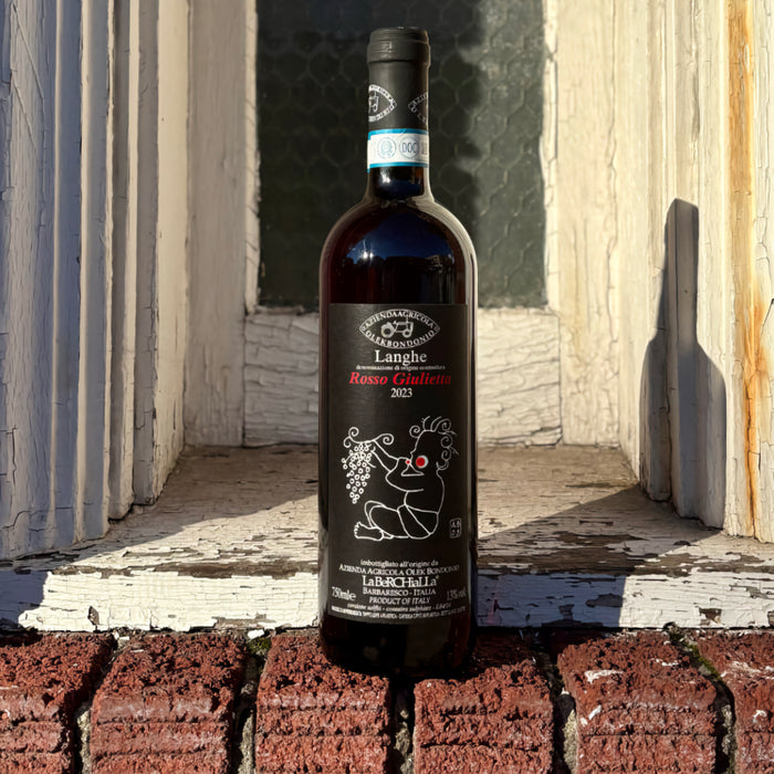 Red wine bottle outdoors with black label and illustrated grape motif.