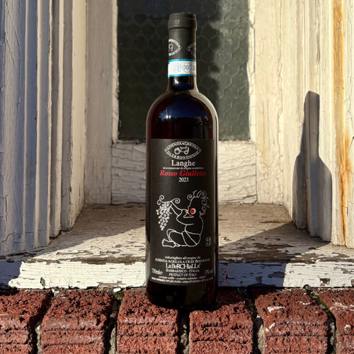 Red wine bottle outdoors with black label and illustrated grape motif.