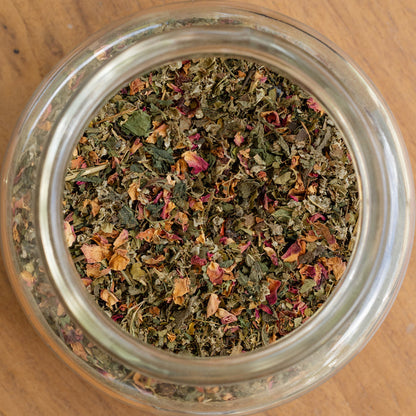 Clear glass jar filled with dried herbs on a wooden surface