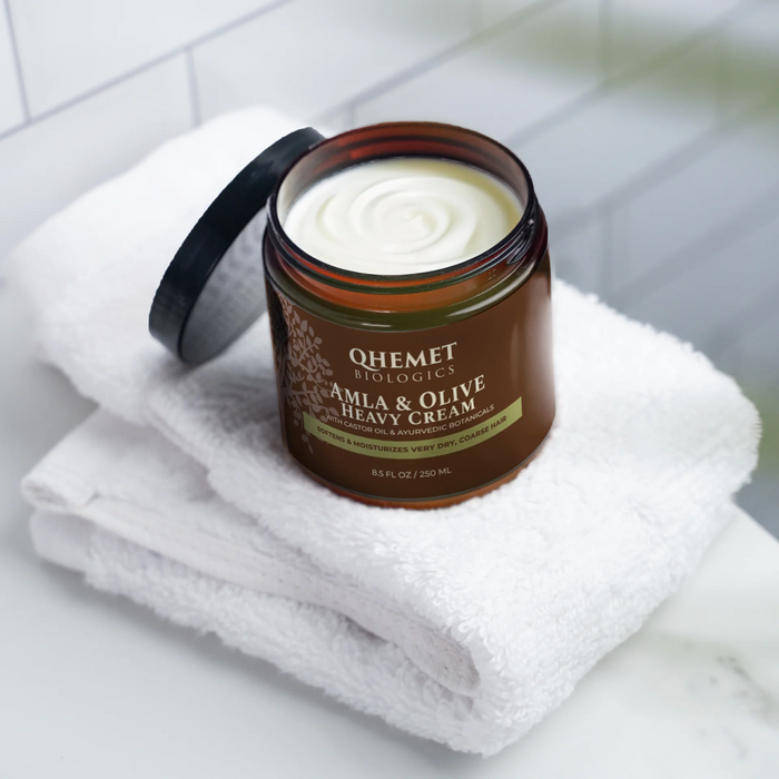 Jar of Qhemet Biologics Amla & Olive Heavy Cream on a white towel with a tiled wall background