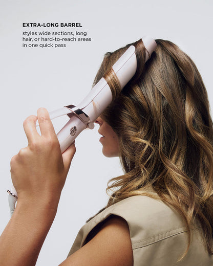 Person using a hair styling tool with an extra-long barrel on a plain background