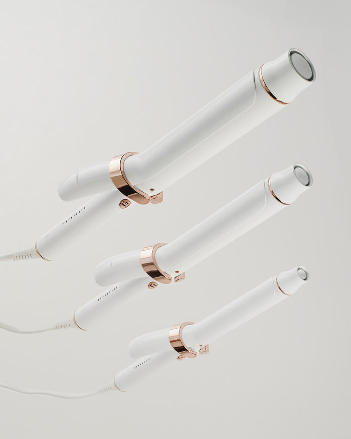 Set of white hair styling tools with rose gold accents on a light gray background