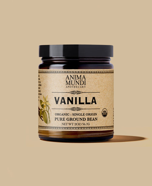 A jar of Anima Mundi Apothecary Vanilla Pure Ground Bean on a solid beige background. The product is in a dark amber glass jar with a black lid and a beige label featuring black text and a vanilla bean illustration.