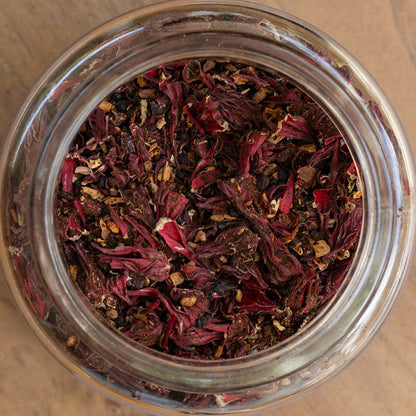 Close-up of a glass jar filled with dried red and brown herbs on a wooden surface.